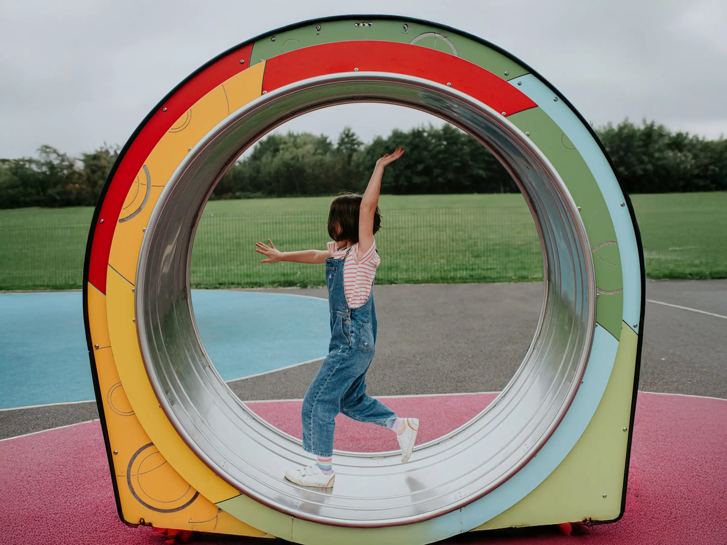 Child playing inside a colorful circular playground structure outdoors